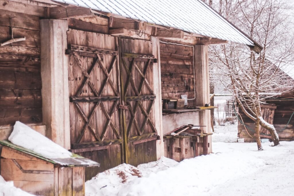 A rustic wooden barn stands amidst snow-covered landscape in Poland, showcasing winter's serene beauty.