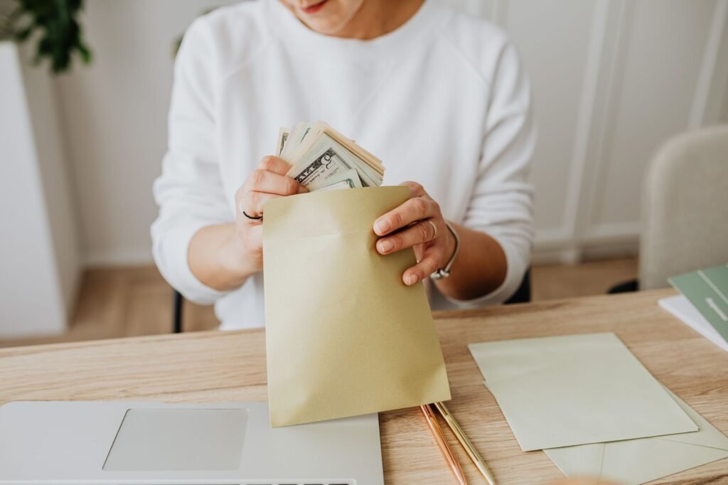Close-up of person holding envelopes with cash at a wooden desk indoors.