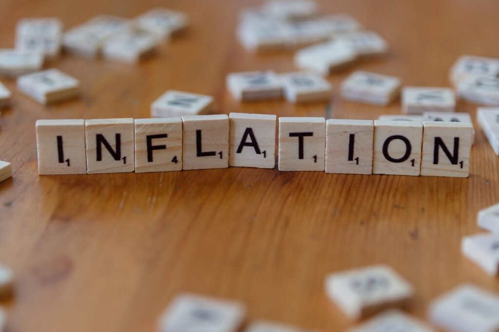 Peças de Scrabble com a palavra "INFLAÇÃO" escritas sobre uma mesa de madeira, simbolizando conceitos econômicos.