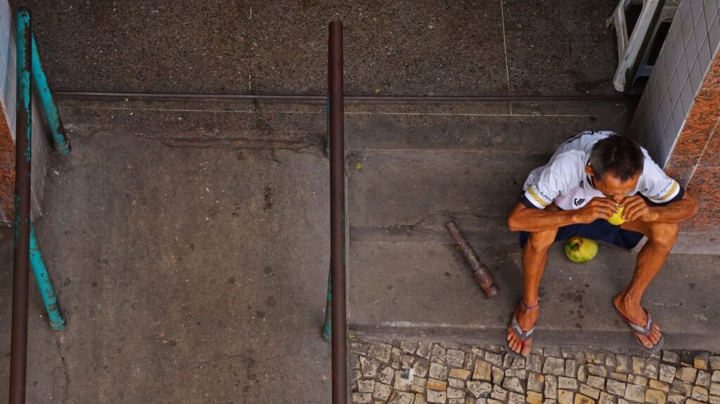 Um homem sentado em degraus urbanos comendo fruta, capturado de cima em Fortaleza, Brasil.