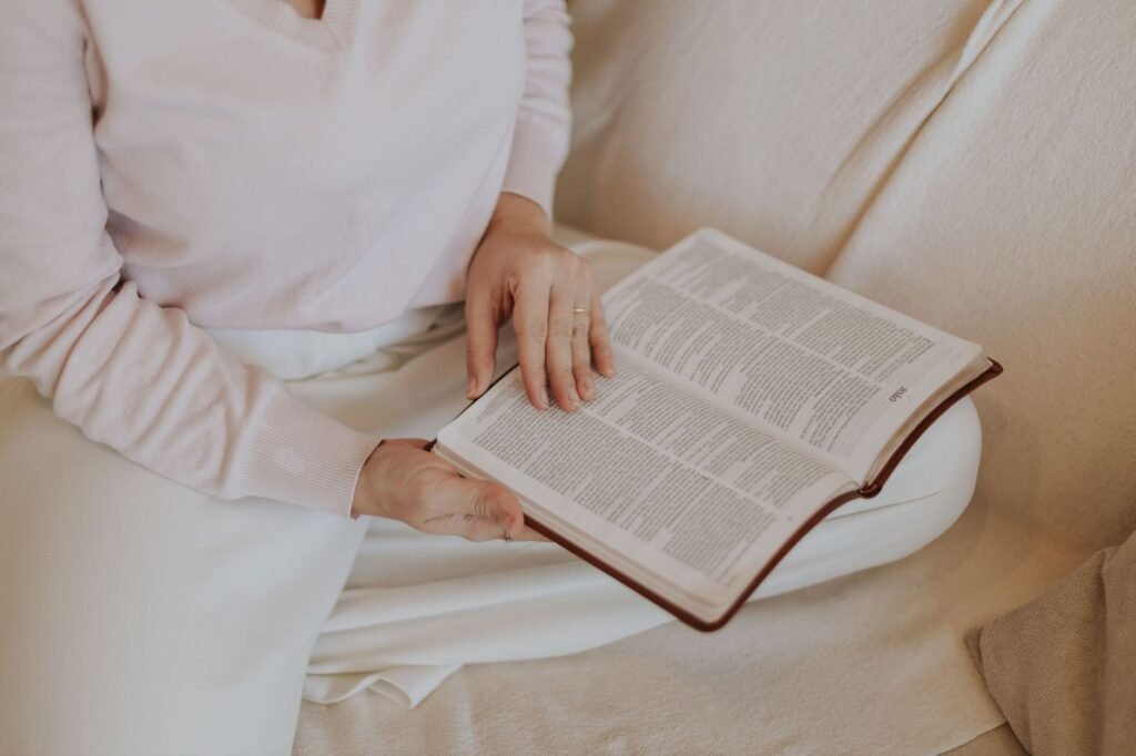 Uma mulher lendo um livro confortavelmente em um sofá, destacando relaxamento e autocuidado.
