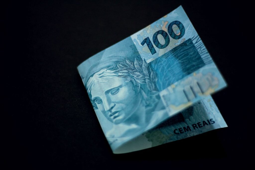 Uma nota de 100 reais brasileira exibida contra um fundo preto, destacando seu design e cor.